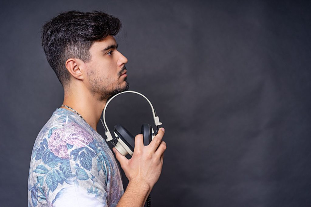 Side view portrait of a man holding headphones in a studio setting against a dark background.