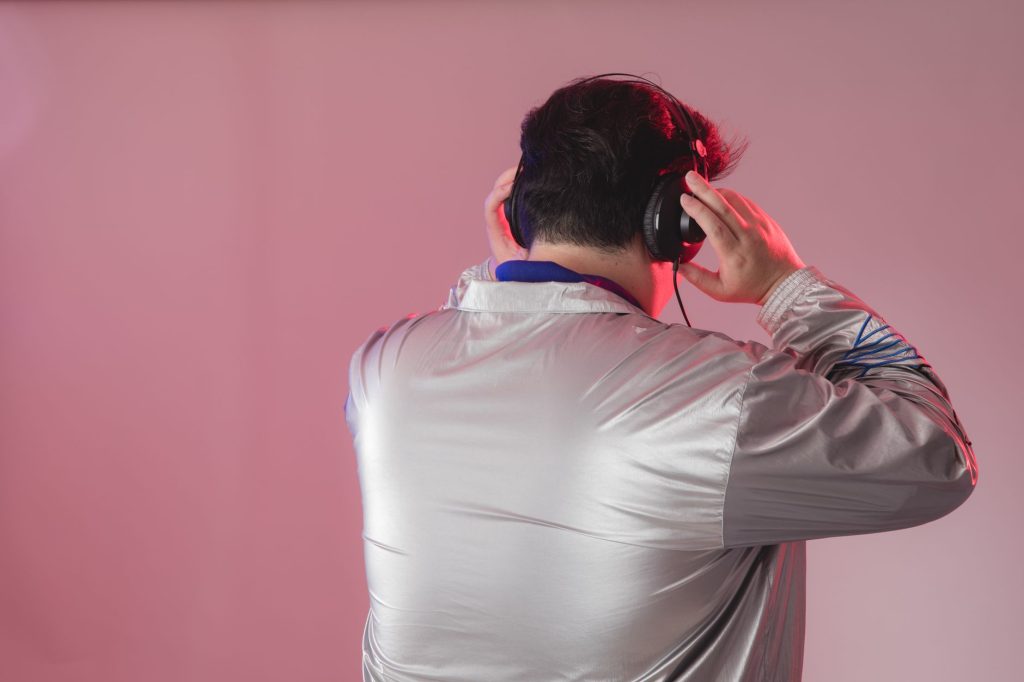 Young man wearing headphones in a studio setting, enjoying music against a pink background.