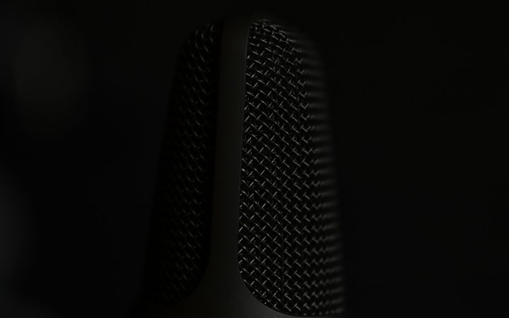 A detailed macro shot of a microphone in a studio setting with a dark background.