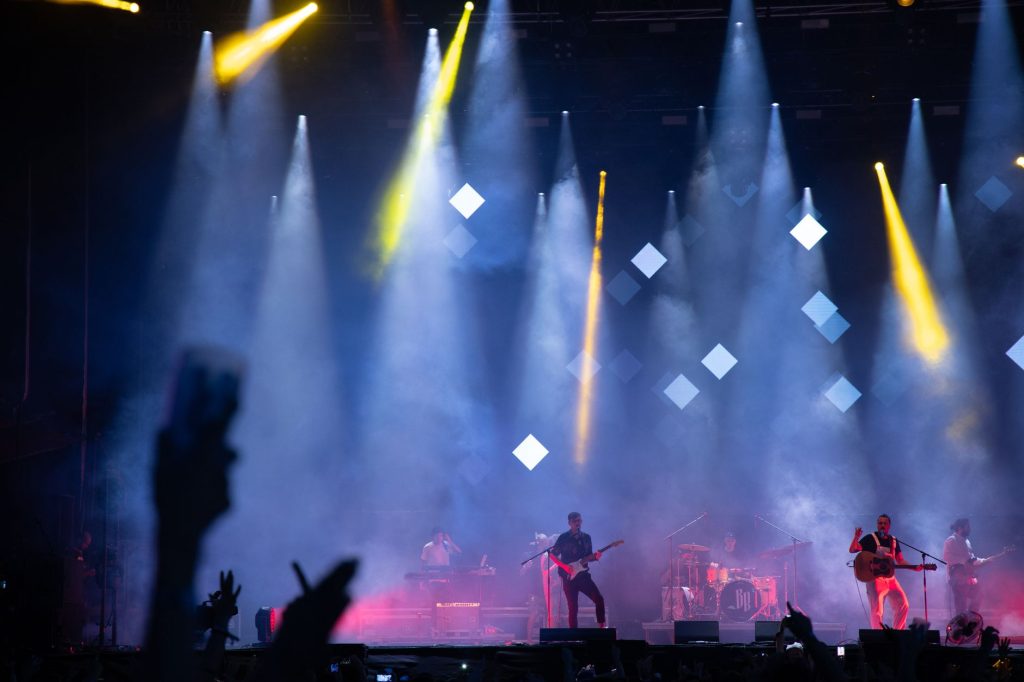 Energetic live performance featuring a band on stage under vibrant lights and smoke effects.