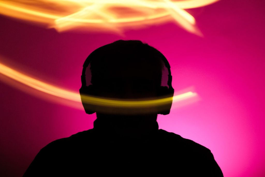 Silhouette of person with headphones against vibrant pink background and dynamic light streaks.