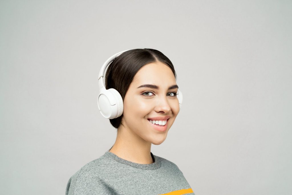 A woman wearing white wireless headphones, smiling and enjoying music indoors.