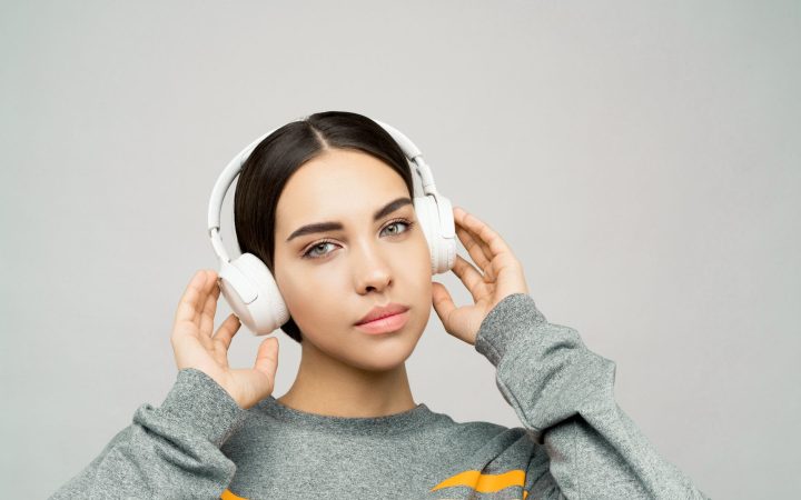 Portrait of a woman in a gray sweater, listening to music with white wireless headphones.