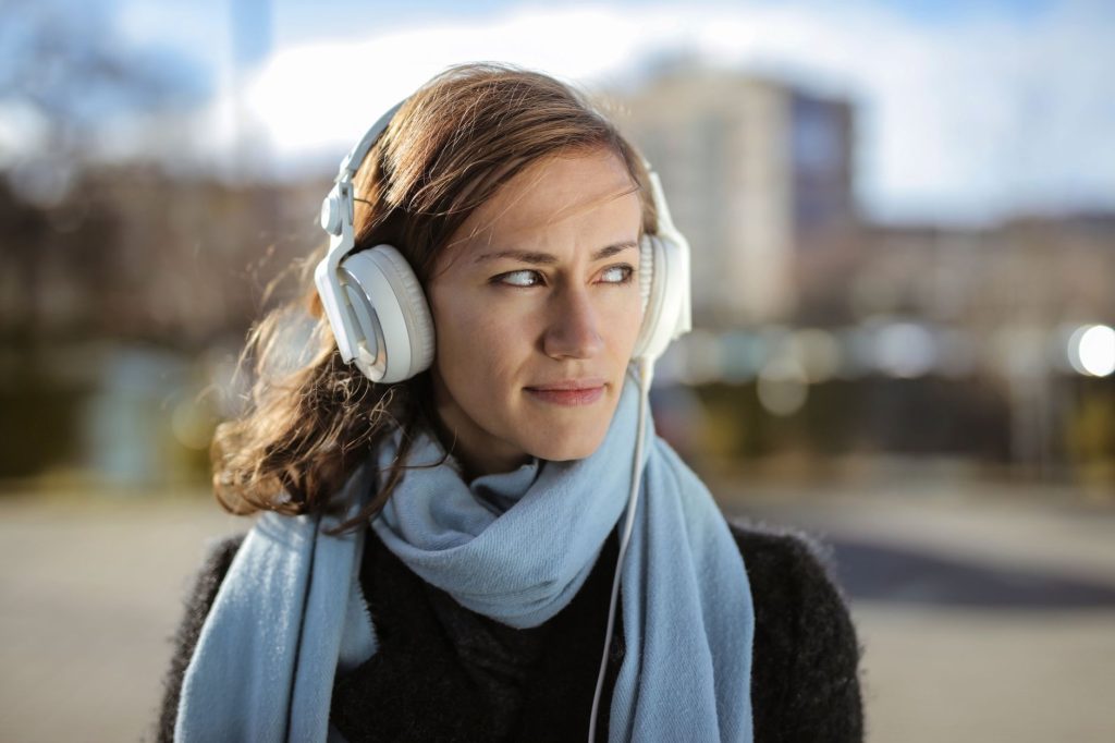 Young woman with headphones and scarf enjoying music outdoors on a sunny winter day.