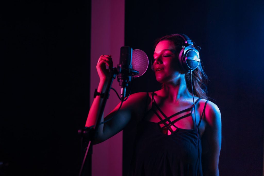 Female singer with headphones singing in a dimly lit recording studio.