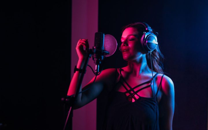 Female singer with headphones singing in a dimly lit recording studio.