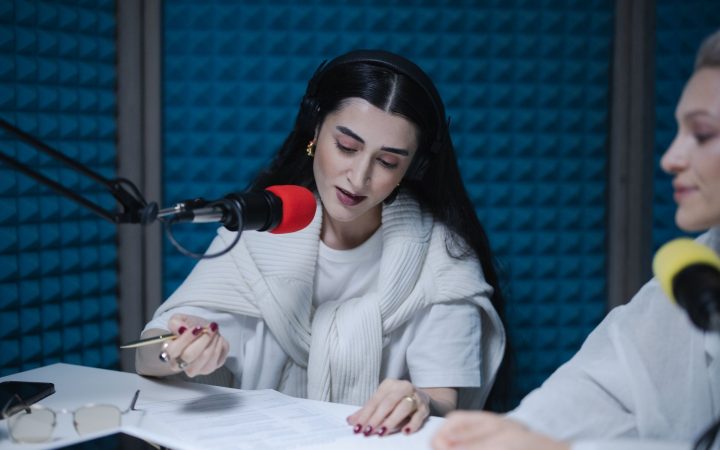 Two women hosting a radio show, using professional microphones in a soundproof studio.