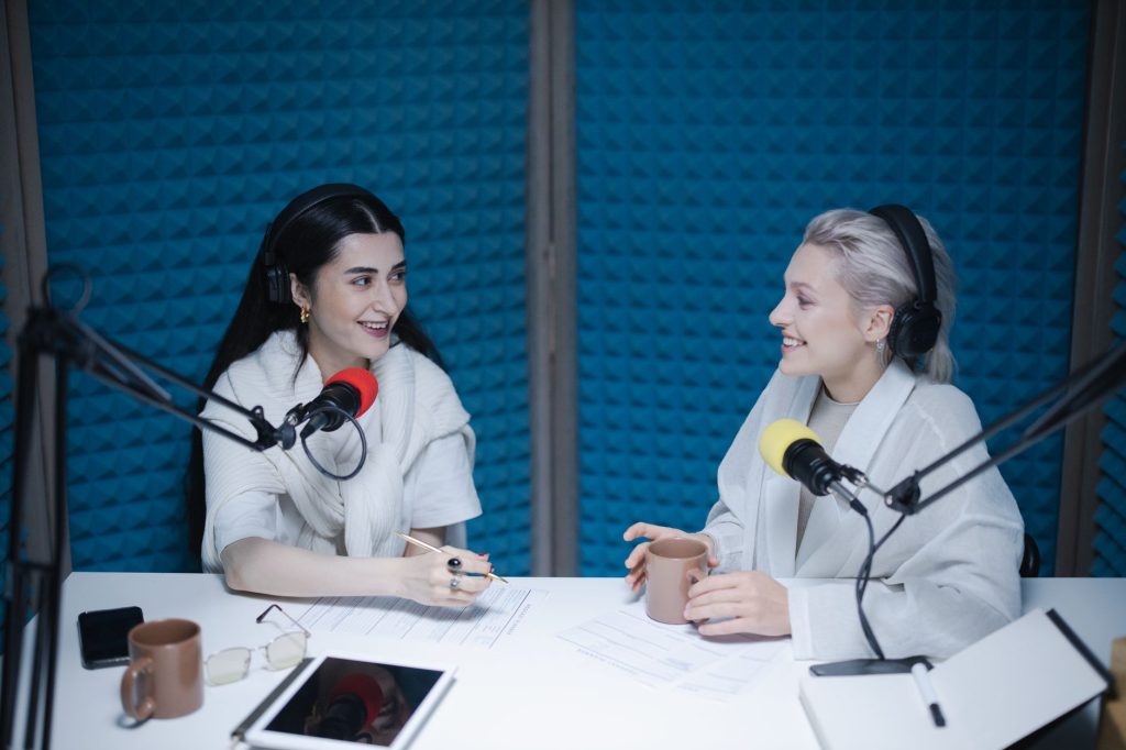 Two women engaged in a lively podcast discussion inside a professional studio setting.