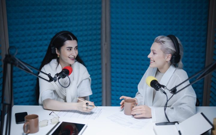 Two women engaged in a lively podcast discussion inside a professional studio setting.