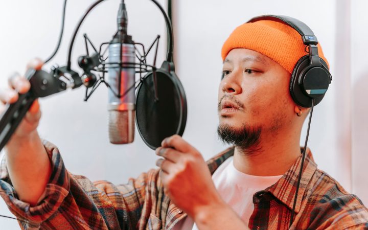 Asian man in studio adjusting microphone while wearing headphones. Ideal for music and recording themes.