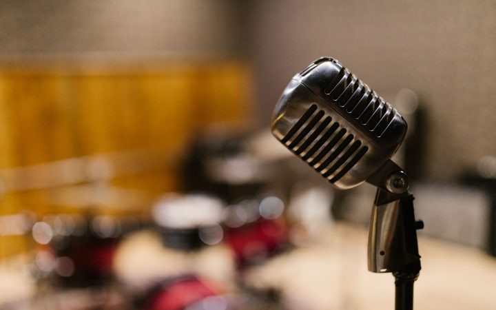 Close-up of a vintage microphone in a music studio with blurred drum set in the background.