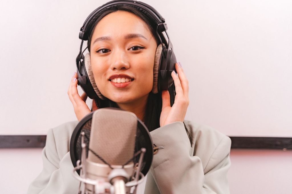 Female artist recording music in studio with condenser microphone and headphones.