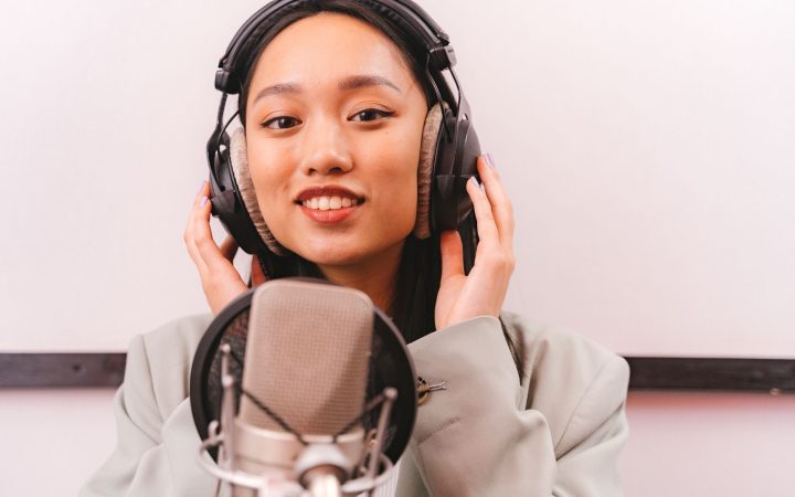 Female artist recording music in studio with condenser microphone and headphones.
