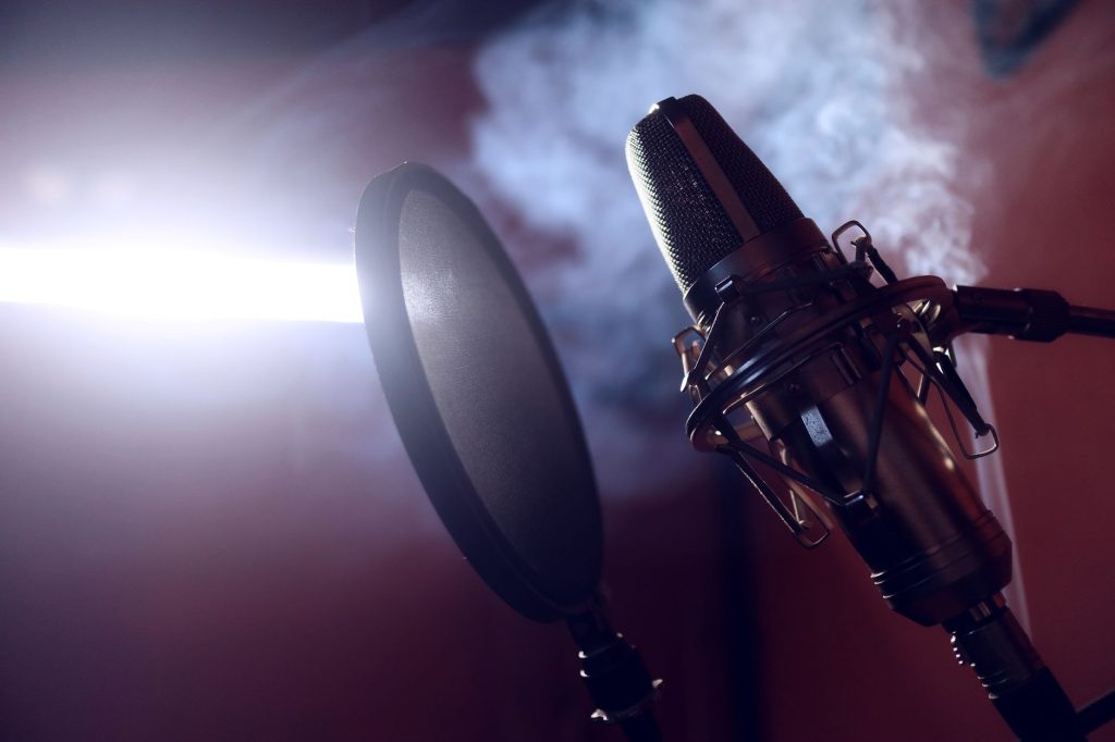 Close-up of a condenser microphone and pop filter in a smoke-filled recording studio.