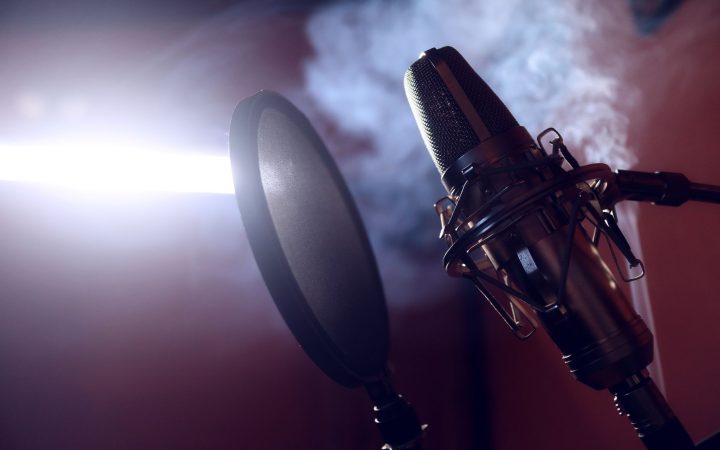 Close-up of a condenser microphone and pop filter in a smoke-filled recording studio.