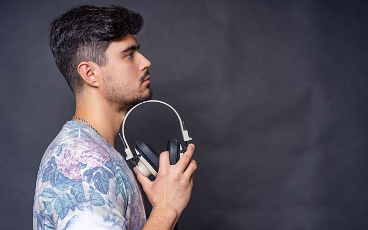Side view portrait of a man holding headphones in a studio setting against a dark background.