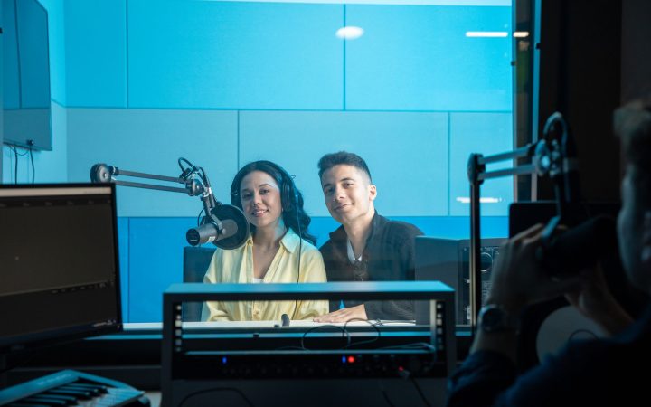 Two people in a radio studio broadcasting a show, featuring professional equipment and microphones with a blue theme.