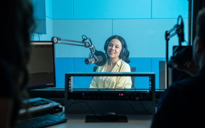 A podcast host records a show in a professional radio studio with microphones and headphones.