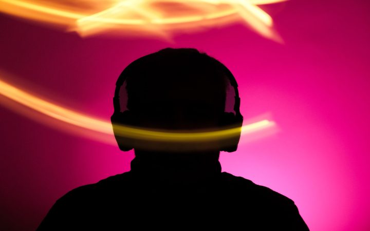 Silhouette of person with headphones against vibrant pink background and dynamic light streaks.