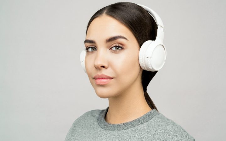 Young woman wearing headphones, posing in a studio setting with a gray background.