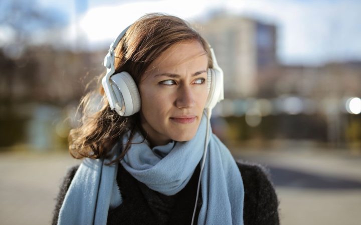 Young woman with headphones and scarf enjoying music outdoors on a sunny winter day.
