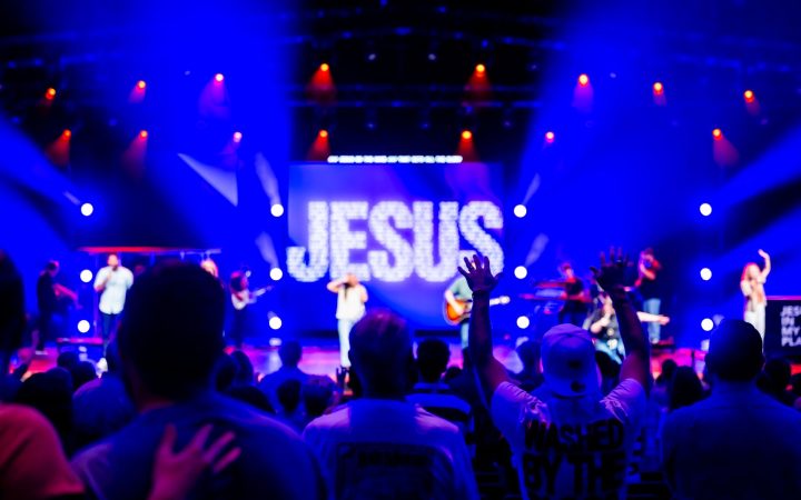 Lively religious concert with a band and audience worshipping under colorful stage lights.