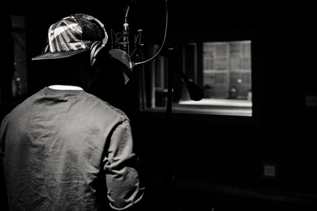 A male singer recording vocals in a black and white studio setting with professional condenser microphones.
