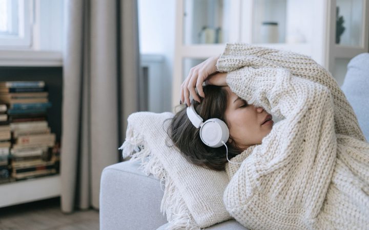 A young woman in a knitted sweater relaxing with headphones, conveying a sense of calm and introspection.