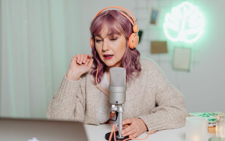 Woman podcaster in a cozy room speaking into a microphone, wearing headphones.