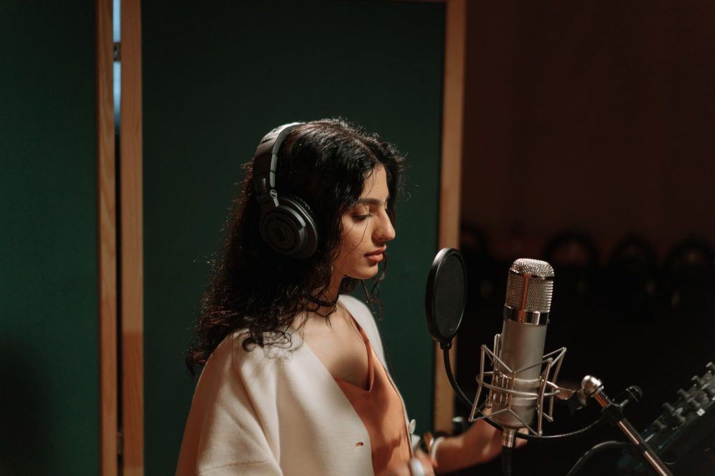 A female singer recording vocals in a professional music studio with a microphone.