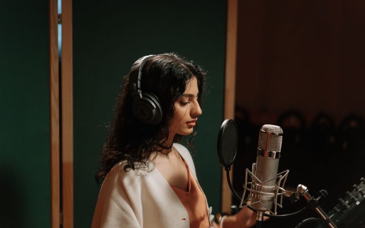 A female singer recording vocals in a professional music studio with a microphone.