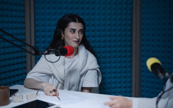 A woman in a podcast studio with microphones and headphones, focused on a discussion.