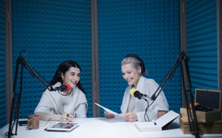 Two women recording a podcast in a soundproof studio with professional equipment.
