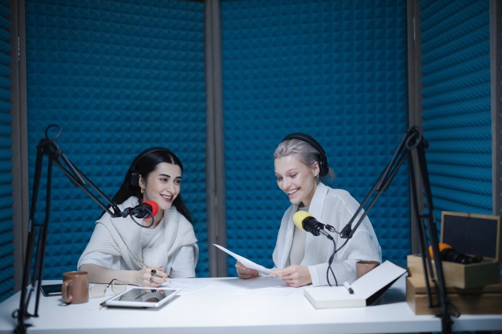 Two women recording a podcast in a soundproof studio with professional equipment.
