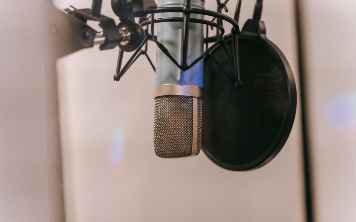 Close-up of a condenser microphone with pop filter in a studio setting, ideal for audio and podcasting.
