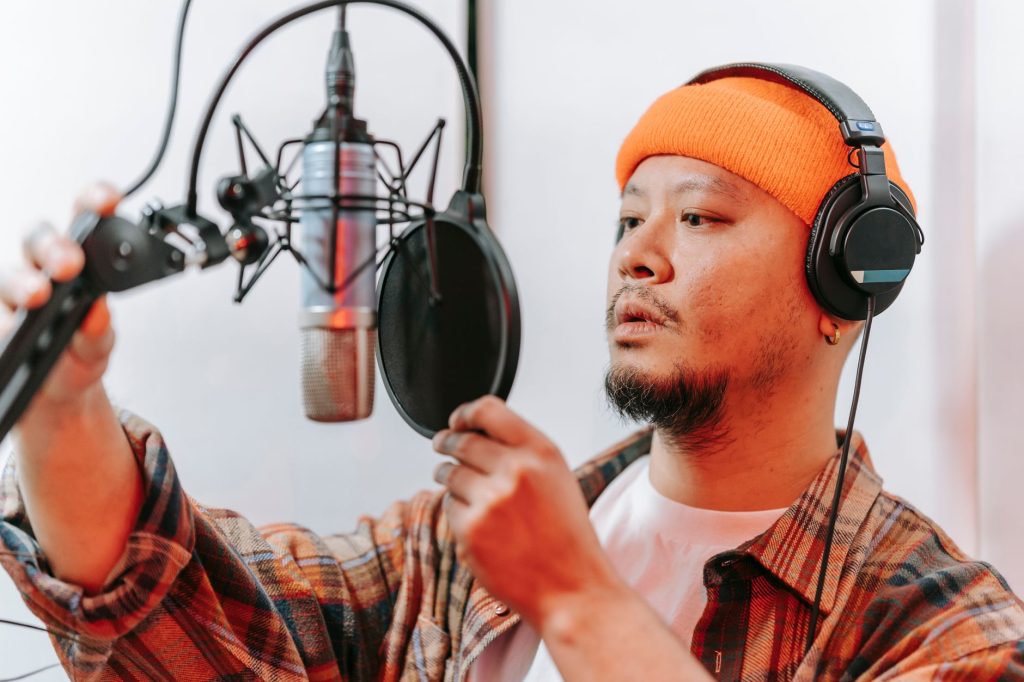 Asian man in studio adjusting microphone while wearing headphones. Ideal for music and recording themes.