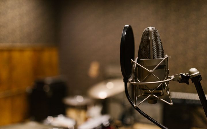 Close-up of a condenser microphone with a pop filter in a recording studio setting.