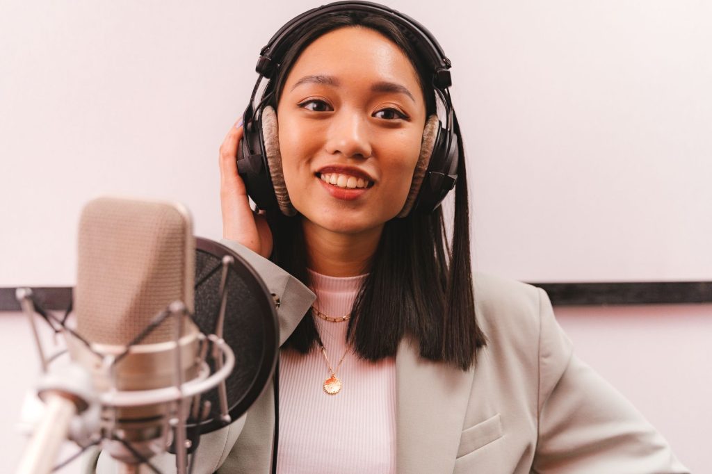 Smiling woman in a studio wearing headphones and speaking into a microphone for a podcast.
